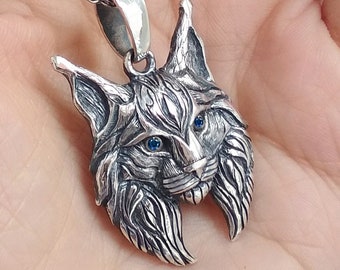 May include: A silver pendant necklace featuring a detailed lynx head with blue eyes. The pendant is attached to a silver chain.