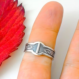 May include: A silver ring with a Celtic knot design and a textured band. The ring is worn on a finger.