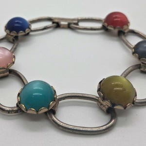 May include: A vintage bracelet featuring a series of oval links connected by round links. Each oval link holds a colorful, domed stone in shades of blue, pink, red, gray, turquoise, and yellow. The bracelet has a silver-tone metal finish.
