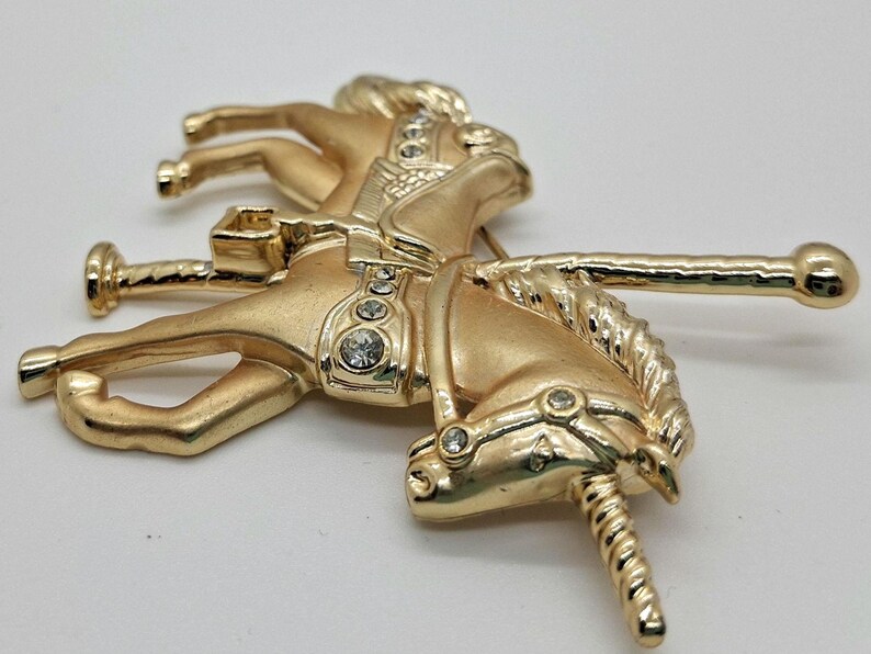 以下が含まれることがあります： 透明なラインストーンのアクセントが付いた、金色のメリーゴーランドの馬のブローチ。 ヴィンテージスタイルのピンは、なびくたてがみと装飾的なサドルを備えた馬の詳細なデザインが特徴です。 ブローチはクラシックなアクセサリーです。