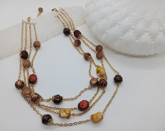May include: A multi-strand gold chain necklace with brown, red, and yellow beads. The beads are various shapes and sizes, including round, square, and oval.