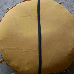 May include: A round, mustard yellow floor cushion with a black stripe down the centre and white tassels around the edge.