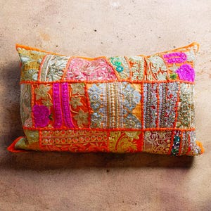May include: A colorful patchwork pillow with orange, pink, and gold embroidery. The pillow is made of different fabrics and has a unique, bohemian style.