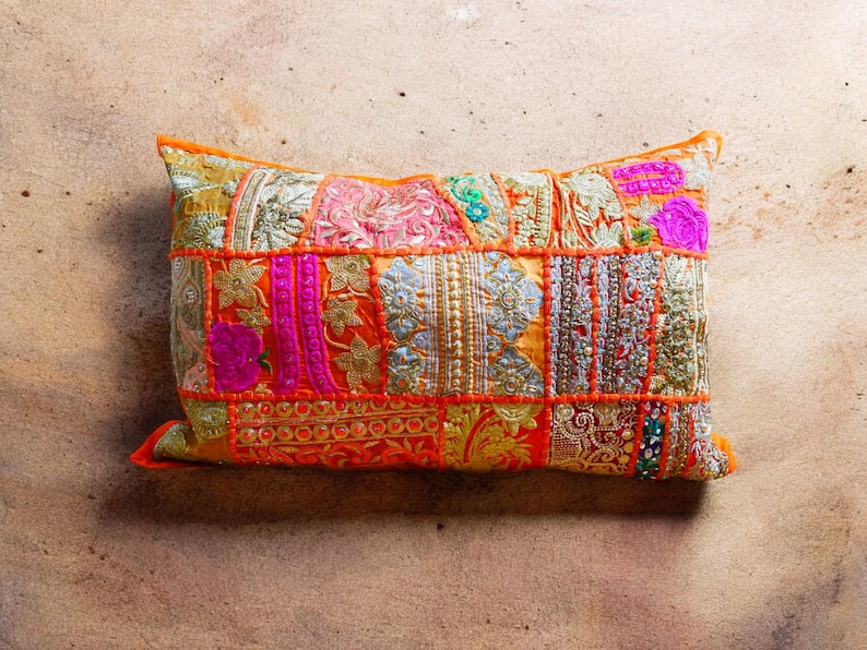 May include: A colorful patchwork pillow with orange, pink, and gold embroidery. The pillow is made of different fabrics and has a unique, bohemian style.