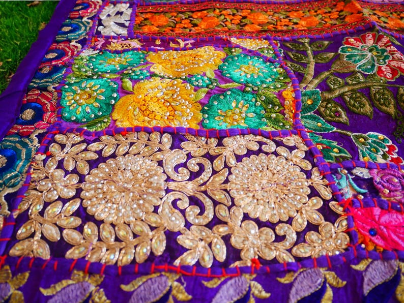 May include: A colorful patchwork quilt with intricate embroidery and sequins. The quilt is made of various fabrics in shades of purple, green, yellow, orange, and red. The quilt is decorated with floral patterns and beaded accents.
