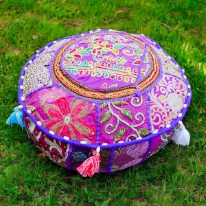 Peut inclure: Un coussin de sol rond, violet et rose, avec un motif patchwork. Le coussin est fait de différents tissus avec des motifs floraux brodés et des paillettes.