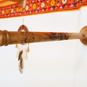 May include: A wooden towel rack with a natural finish, mounted on a white wall. The rack features carved leaf designs and a decorative end. The design is rustic and handcrafted, suitable for a bathroom or kitchen.
