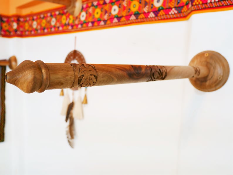 May include: A wooden towel rack with a natural finish, mounted on a white wall. The rack features carved leaf designs and a decorative end. The design is rustic and handcrafted, suitable for a bathroom or kitchen.