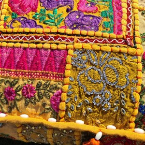 May include: A colorful patchwork cushion cover with intricate embroidery and sequins. The cover features a variety of floral patterns and geometric designs in shades of pink, yellow, blue, and green.