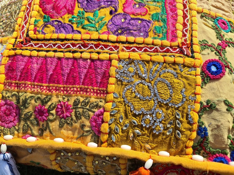 May include: A colorful patchwork cushion cover with intricate embroidery and sequins. The cover features a variety of floral patterns and geometric designs in shades of pink, yellow, blue, and green.