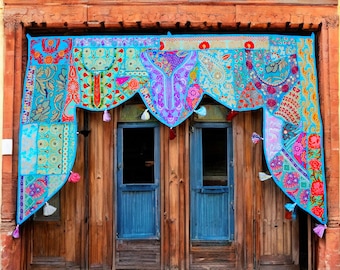 May include: A colorful, patchwork fabric valance hangs above two blue doors. The valance features a variety of patterns in shades of turquoise, pink, purple, and orange, with tassel accents. The wooden door frame is a warm brown.