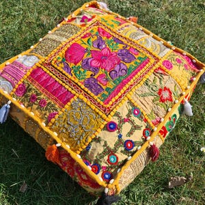 May include: A yellow, pink, and green patchwork floor cushion with embroidered floral designs and tassels.