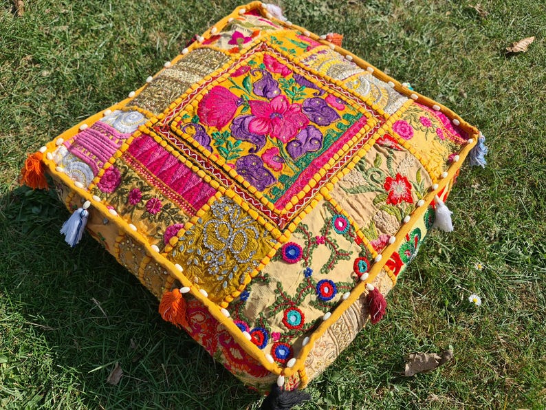 May include: A yellow, pink, and green patchwork floor cushion with embroidered floral designs and tassels.