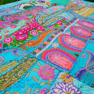 May include: A vibrant, patchwork textile featuring a mix of colors including turquoise, pink, orange, and gold. The design incorporates floral and paisley patterns, with intricate embroidery and beadwork. The textile is likely a decorative item, such as a quilt or throw.