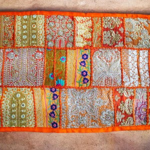 May include: A colorful patchwork throw pillow with an orange border and intricate embroidery. The pillow is made of various fabrics and features a variety of colors, including gold, red, and blue.