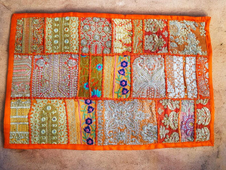 May include: A colorful patchwork throw pillow with an orange border and intricate embroidery. The pillow is made of various fabrics and features a variety of colors, including gold, red, and blue.