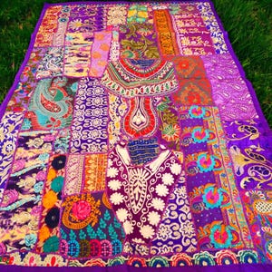Op de afbeelding: Een kleurrijk patchwork-deken met een paarse achtergrond. Het deken is gemaakt van verschillende stoffen met bloemen- en paisleypatronen. Het deken is versierd met borduurwerk en pailletten.