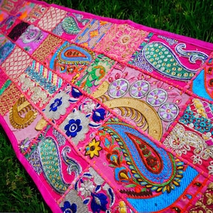 Könnte beinhalten: Ein rosafarbener Patchwork-Läufer mit bunten Stickereien und Pailletten. Der Läufer besteht aus verschiedenen Stoffen und zeigt Paisley-Muster, Blumenmotive und geometrische Formen.
