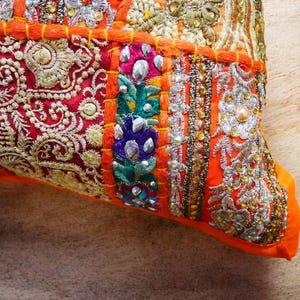 May include: Orange and red patchwork cushion cover with intricate embroidery and beaded details. The cushion cover is made of a variety of fabrics and features a mix of colors and textures.