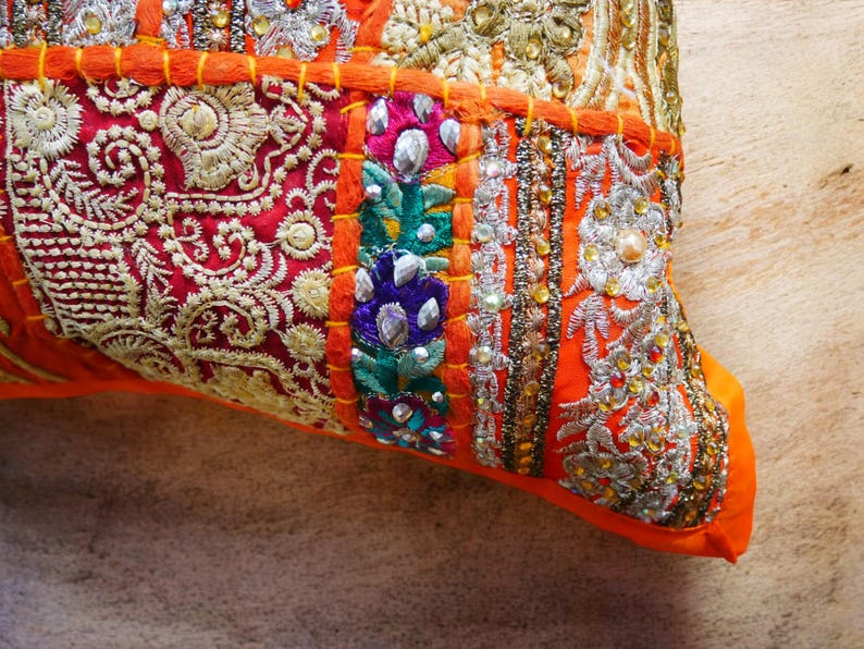 May include: Orange and red patchwork cushion cover with intricate embroidery and beaded details. The cushion cover is made of a variety of fabrics and features a mix of colors and textures.