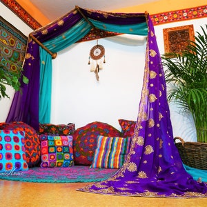 May include: A bohemian-style seating area with a canopy draped in purple and teal fabric. Colorful pillows in various patterns and a round rug create a cozy space. A dreamcatcher hangs from the canopy.