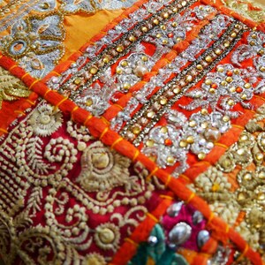 May include: A colorful patchwork cushion cover with intricate embroidery and beaded details. The fabric is a mix of orange, red, and gold, with a variety of patterns and textures.
