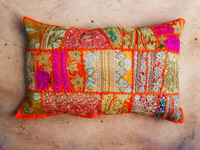 May include: A colorful patchwork pillow with a mix of orange, pink, yellow, and green fabrics. The pillow is decorated with intricate embroidery and sequins.
