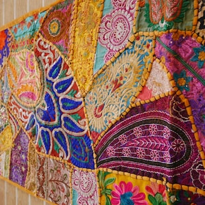 Könnte beinhalten: Ein bunter Patchwork-Tischläufer mit aufwendigen Stickereien und Pailletten. Der Läufer besteht aus verschiedenen Stoffen in den Farben Rosa, Lila, Blau, Grün, Gelb und Orange.