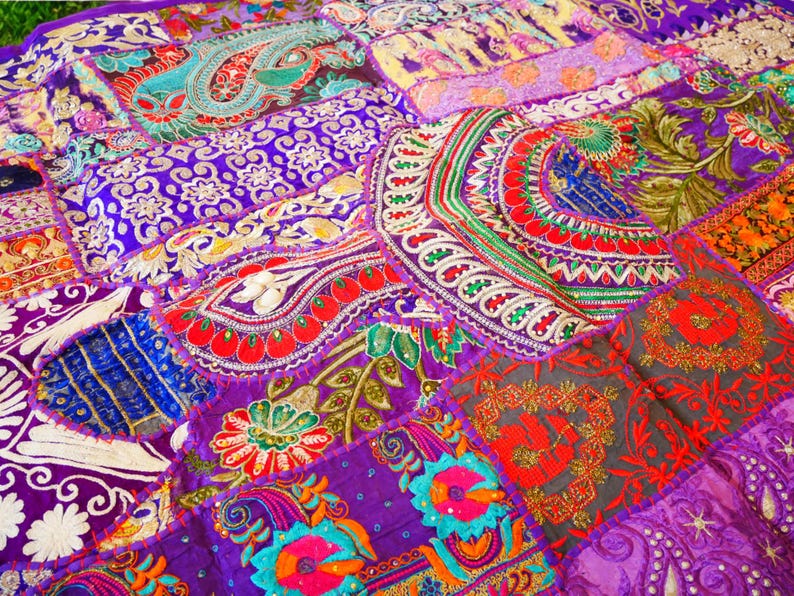 May include: A colorful patchwork quilt with a variety of floral and geometric patterns in shades of purple, red, green, and blue. The quilt is made of different fabrics and textures, and it has a unique and bohemian style.