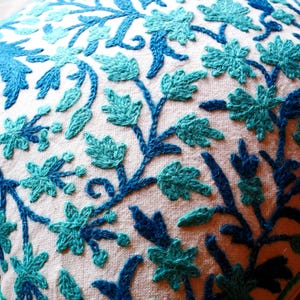 Peut inclure: Un coussin blanc avec des motifs floraux brodés bleus et turquoise.