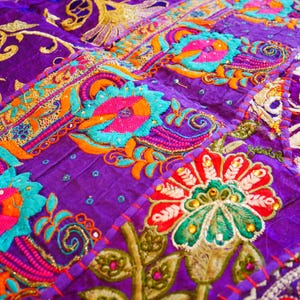 May include: A purple fabric patchwork with colorful embroidered flowers and intricate designs. The fabric is decorated with sequins and beads.