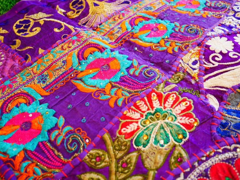 May include: A purple fabric patchwork with colorful embroidered flowers and intricate designs. The fabric is decorated with sequins and beads.