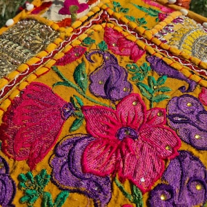 May include: A close-up of a colorful embroidered fabric with a yellow background. The fabric features a floral design with pink, purple, and green accents. The fabric is stitched with a variety of different colored threads.