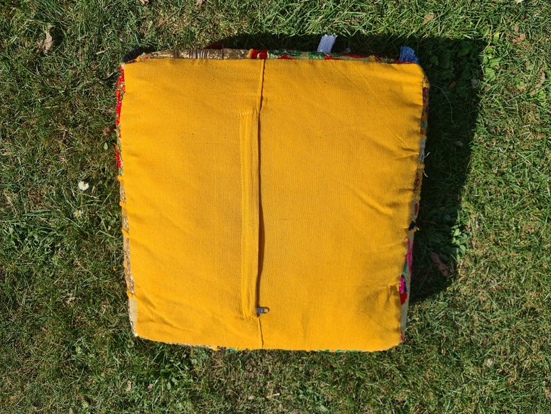 May include: A yellow square cushion with a zipper closure. The cushion is made of a patchwork fabric with colorful floral patterns.