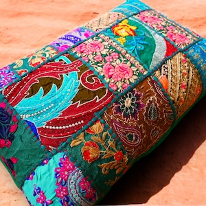 Op de afbeelding: Een patchwork kussen met een groene achtergrond en kleurrijke geborduurde ontwerpen. Het kussen is gemaakt van verschillende stoffen en texturen, waaronder fluweel, zijde en katoen. De borduursels bevatten bloemmotieven, paisley-ontwerpen en geometrische vormen.