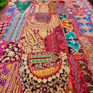 Può includere: Un quilt colorato a patchwork con ricamente ricamato e accenti dorati. Il quilt è realizzato con vari tessuti in tonalità di rosa, viola, rosso, blu e verde.