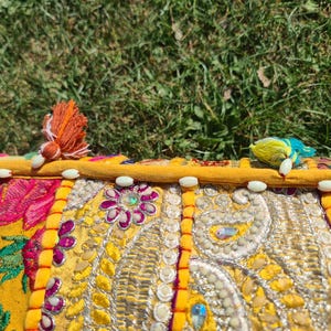 May include: A yellow, pink, and green patchwork cushion with white beads around the edge. The cushion is decorated with embroidered flowers and paisley patterns.