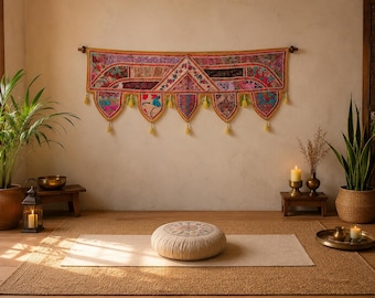 May include: A rectangular wall hanging featuring a patchwork of vibrant fabrics in shades of pink, gold, and purple, adorned with intricate embroidery and small yellow tassels along the bottom edge, positioned above a round, beige floor cushion.