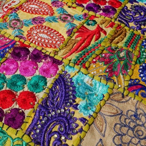 May include: A colourful patchwork fabric with intricate embroidery and sequins. The fabric is made up of different squares of fabric, each with a different design. The fabric is a vibrant mix of colours, including red, green, blue, yellow, and purple.