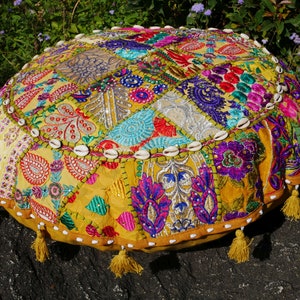 May include: A round, yellow, patchwork floor cushion with colourful embroidery and white shell accents. The cushion has tassels around the edge.