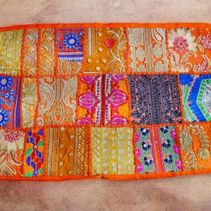 May include: A colorful patchwork cushion cover with an orange border. The cover is made of various fabrics with intricate embroidery and sequins in shades of gold, pink, blue, and green.