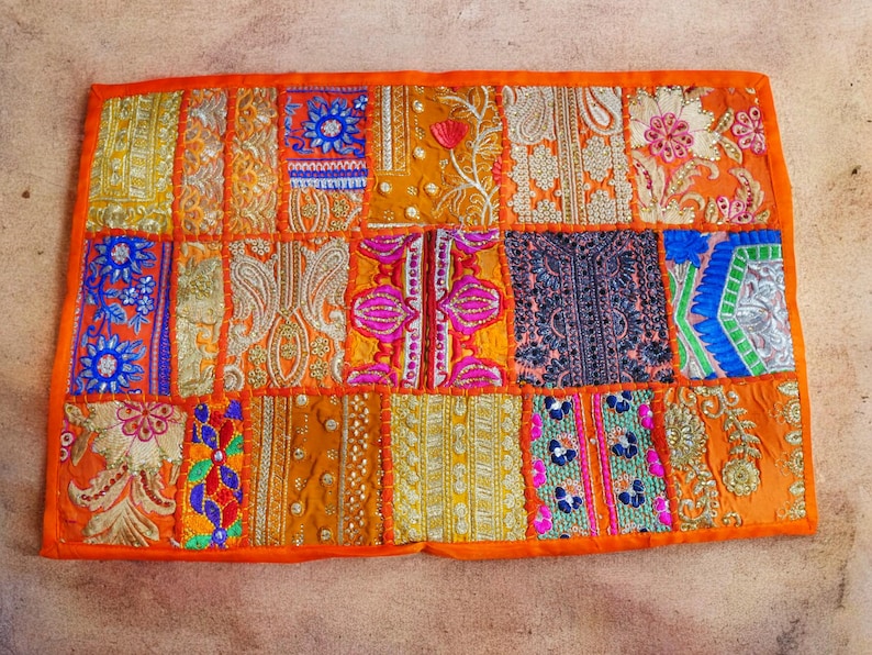 May include: A colorful patchwork cushion cover with an orange border. The cover is made of various fabrics with intricate embroidery and sequins in shades of gold, pink, blue, and green.