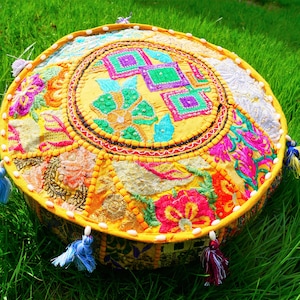 Könnte beinhalten: Runder, farbenfroher Bodenkissen mit Patchwork-Design. Das Kissen hat eine gelbe Mitte mit gestickten Blumen- und geometrischen Mustern in Rosa, Grün und Lila. Es hat einen gelben Rand und ist mit Quasten in verschiedenen Farben verziert.