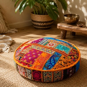 May include: A round floor cushion featuring a vibrant patchwork design with various embroidered fabrics in shades of orange, pink, blue, and yellow. The cushion has a solid orange fabric border and a multi-coloured patterned side panel.