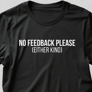 Pode incluir: T-shirt preto com o texto branco "NO FEEDBACK PLEASE (EITHER KIND)". A camisa tem mangas curtas e gola redonda. O texto está centralizado na frente da camisa.