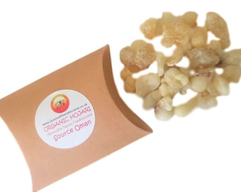 Puede incluir: Un primer plano de una pequeña bolsa de resina de incienso Hojari orgánico. La bolsa es marrón y tiene una etiqueta blanca con el texto "Organic Hojari (Boswellia Sacra) Frankincense Source Oman" y un logotipo con un ojo dentro de un círculo.