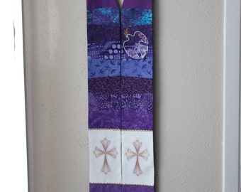 May include: A purple and white liturgical stole with a dove and cross design. The stole is made of fabric and has a variety of textures and patterns.