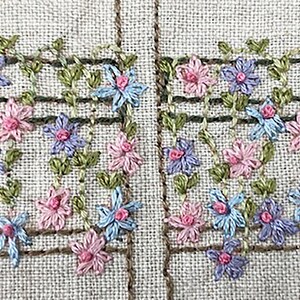 Puede incluir: Primer plano de un dise&ntilde;o floral bordado. El dise&ntilde;o presenta flores rosas, azules y moradas con hojas verdes, dispuestas en un patr&oacute;n de enrejado. El fondo es una tela beige claro con rayas verticales marrones.