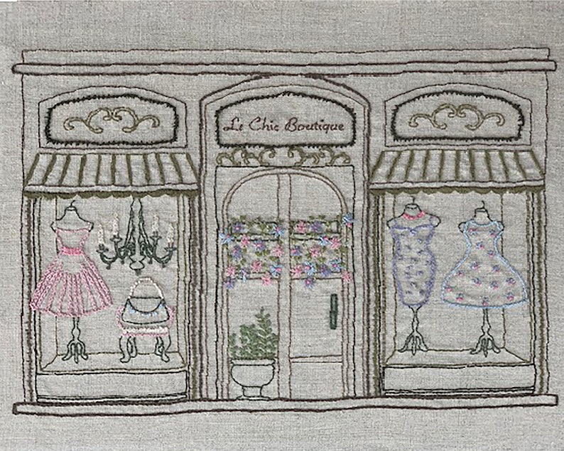 Puede incluir: Imagen bordada de un escaparate de una boutique, con el texto "Le Chic Boutique". La tienda exhibe vestidos en maniqu&iacute;es en los escaparates. Una l&aacute;mpara de ara&ntilde;a cuelga en el interior y detalles florales adornan la puerta y las ventanas, creando una escena encantadora y detallada.