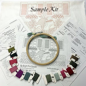 Puede incluir: Un kit de bordado con el texto "Sample Kit" y "My Bright Pink Scooter". El kit incluye un bastidor de bordado de madera, hilo de bordar de varios colores e instrucciones impresas. El dise&ntilde;o presenta un scooter y elementos arquitect&oacute;nicos.